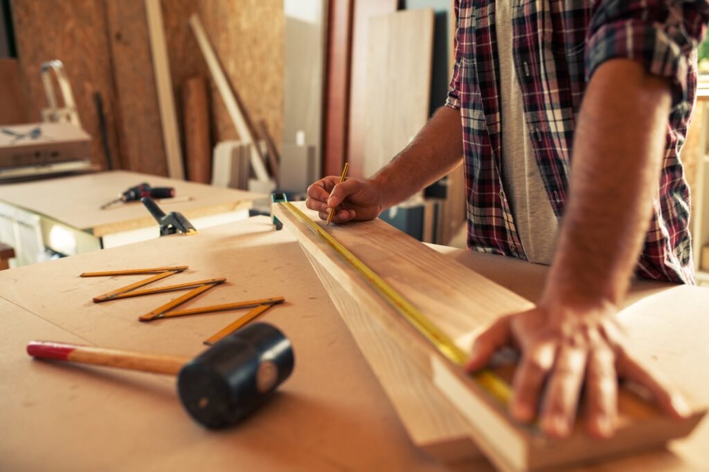 Carpenter measuring a wood board with a tape measure and pencil