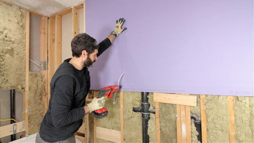 Worker cutting drywall around wall framing