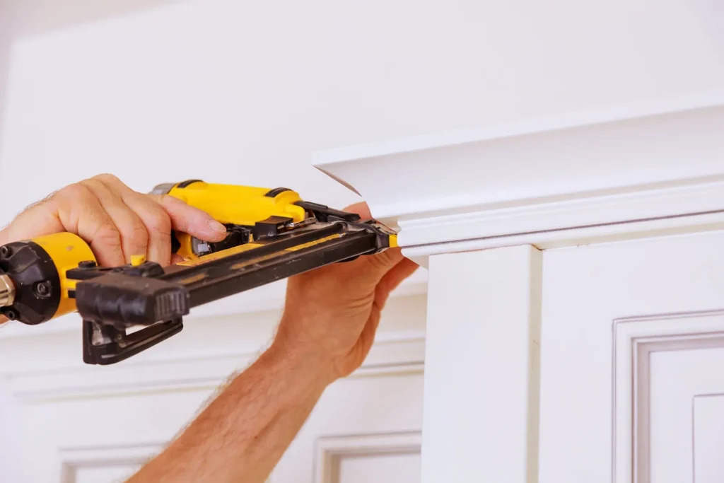 Carpenter nailing white trim molding with a nail gun