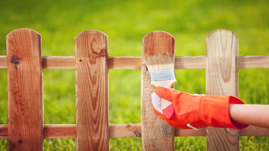 Gloved hand staining a wooden picket fence