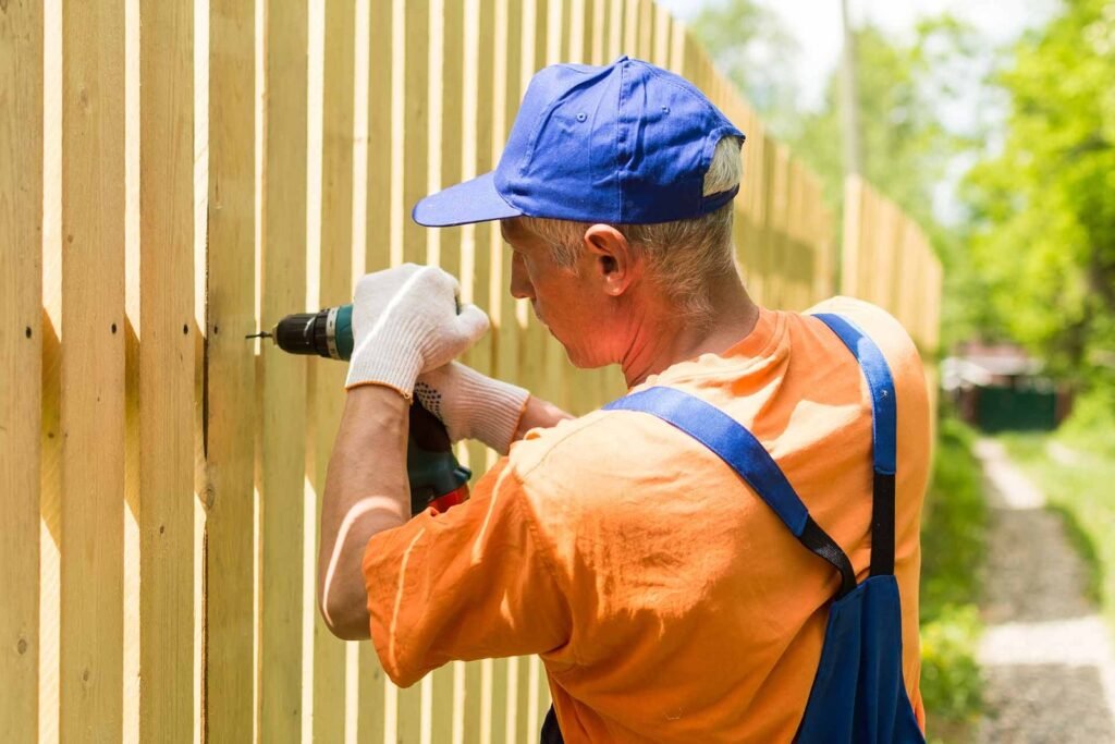 Worker drilling wooden fence boards into place