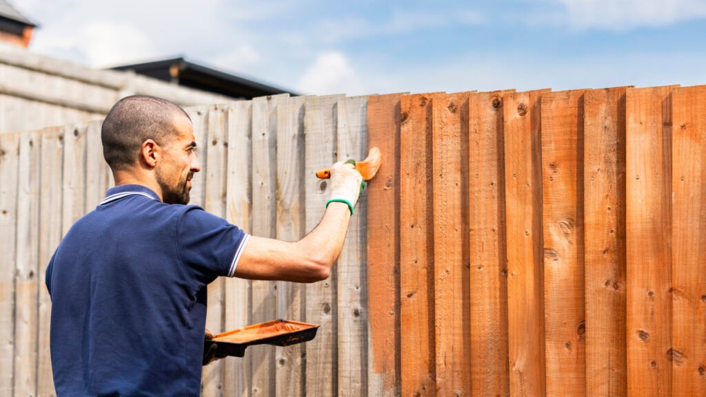 Worker staining a weathered wood fence