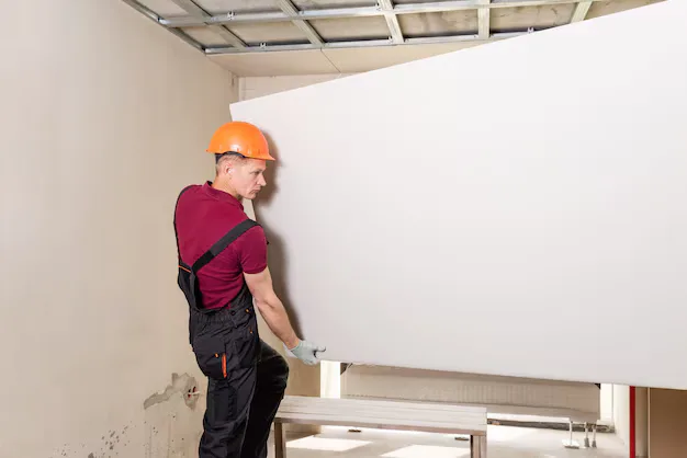 Worker positioning a drywall sheet on a wall
